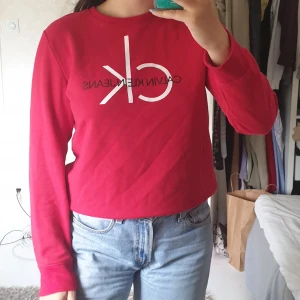 Sweater - Snygg röd Calvin Klein Jeans sweater som är använd en gång. Skön tröja som är mjuk på insidan. Storlek L men fukar på M. Köpes för 550kr i Calvein Klein affär i New York. Du står för frakt. Kan mötas upp beroende på vart.