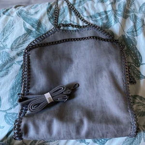 Grå väska med skinimitation - Säljer denna super fina väska som aldrig är använd! Stella McCartney liknande väska! Längd 43cm bredd 38cm djup 28cm! 1 stort fack med 3 små fack i väskan plus 1 utanpå väskan! Axelband ingår! Bud börjat på 200kr! Frakt ingår ej! Buda i kommentarerna
