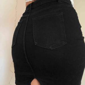 Svart jeanskjol i ganska stretchigt material, en ”split” på baksidan, med fickor 