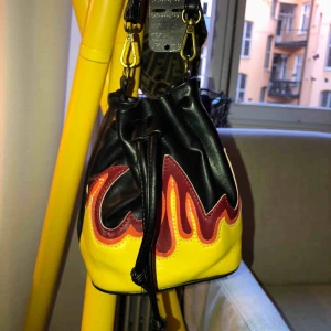  - Liten väska från Bikbok med flammor på. Det är en fake-läderväska och den är i väldigt bra skick.