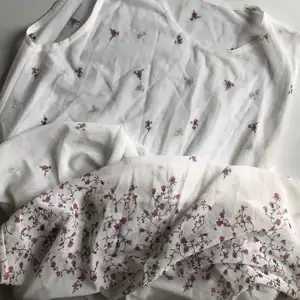 Vit långklänning i mesh-material med rosa blommor spridda över klänningen. Ger ”vacker sommardröm” vibes. Klänningen kan användas över en slipklänning eller som en cover-up. Kan mötas upp eller frakta