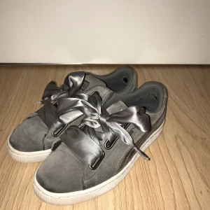 Puma sneakers  - Grå/silvriga låga sneakers från puma med vit sula. Har silkes/satin snören. De är använda & har slitning i hälen (se bild 3), . Nypris är 599kr. Stl 37, passar även en stor 36:a och liten 38:a. Tyget är utav mocka. De mörka på bilden syns inte i verkligheten, de är ljuset!