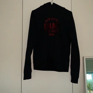 Mörkblå gant hoodie strl 176 ban 16-17 år - Mörkblå hoodie från Gant med röd text fram och huva bak. Säljes pga att den inte kommer till användning. Använd ca 3 ggr.
