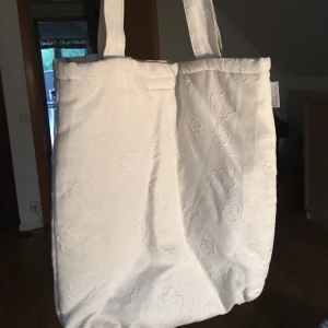 Tygpåse med blommor - Gullig tygpåse i vitt med blommor i mönstret. Påsen är ”fodrad” och med en liten ficka inuti. Perfekt som datorväska eller liknande:) frakten ingår