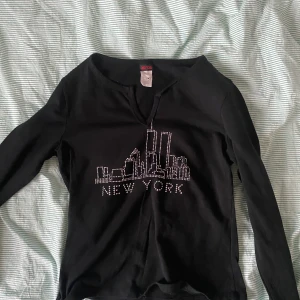 svart Y2k new york topp - Skitsnygg svart långärmad tröja med en siluett av höghus och new york skrivet i rhinestones<3 st L men passar som en M. Köpare står för frakt💖 säljer pga något kort i ärmarna 