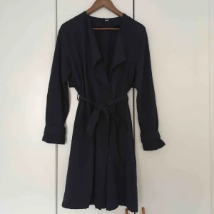  - Tunn mörkblå kappa. Inköpt 2014. Använd under vår och sommar. Fäster med två knappar, ingen dragkedja. Två fickor. Tygband i midjan. I fint skick. Kan mötas upp i Malmö eller Lund, annars tillkommer frakt på 90 kr.
