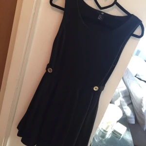  - Supersnygg 'sailor' liknande klänning i svart jersey tyg med guldiga knappar på sidorna både bak och fram. Använd endast 1 gång och i mycket bra skick! 