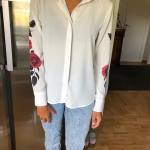 Vit skjorta med rosdetaljer  - Vit skjorta med rosdetaljer. Bra skick. Säljer då den börjar bli för liten. Pris: 80 kr, köparen står för frakten. 