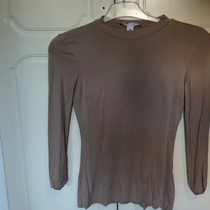 Långärmad tröja i färgen beige från Nelly - Säljer en tunn långärmad tröja från Nelly. Den är i bra skick och plagget sitter bra på kroppen. Den har en hög krage. 