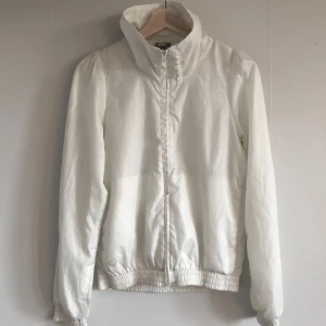  - Vit Nike vindjacka. Fina feminina detaljer, lätt veckade axlar och nätt modell. Två sidfickor. Dubbel kläpp på dragkedja. Endast en minimal fläck på ena ärmen, se sista bilden. Köparen betalar frakt, 45 kr.