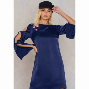  - Marinblå klänning med broderade blommor vid högra bröstkorgen. Från NaKd x Andrea Hedenstedt nypris runt 500kr, kommer ej ihåg. Använd enstaka gånger. Säljer för 100kr + ev frakt.