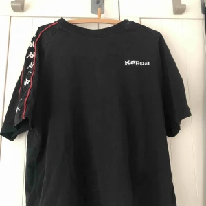  - En svart kappa T-shirt med detaljer på ärmen. Snyggt att vika upp ärmarna samt sätta ner den i jeansen men även snygg att ha den som den är. 