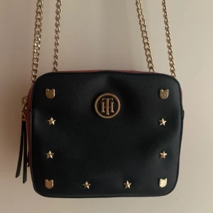 Väska - Väska i fint skick från Tommy Hilfiger. Blå och röd med guldiga detaljer och två fack. Kan bäras på axeln eller som crossbody. 