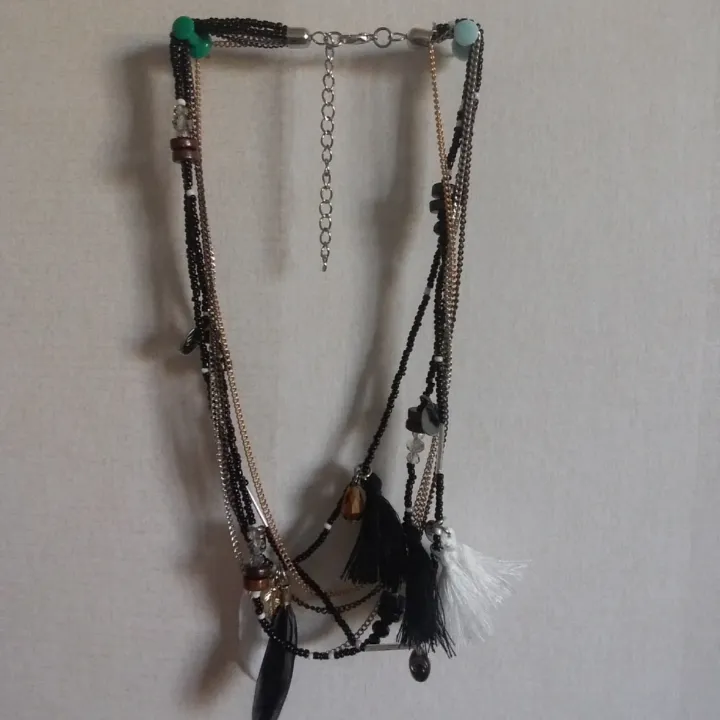 Halsband i flera lager med pärlor fjädrar och toffsar i svart vit silver och guldfärg. Accessoarer.