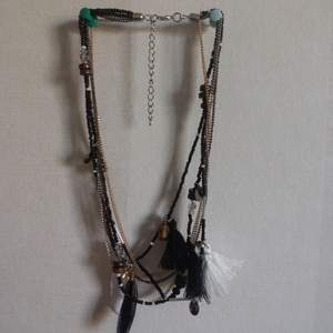 Halsband i flera lager med pärlor fjädrar och toffsar i svart vit silver och guldfärg