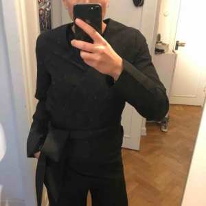  - Svart Omlottkavaj med knytdetalj. Från Wera. Använd 1 gång.  Supersnygg till jeans som till kostymbyxor, ett modernt snitt som adderar lite extra.  