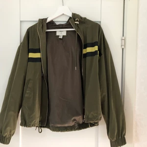Militär grön jacka  - Militärgrön jacka med svarta och gula sträck. Från Forever 21. Tunt material. Storlek M. Hämtas i Lidköping, eventuell frakt betalas av köparen
