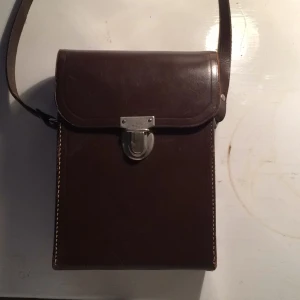  - Superfin väska i hårt material. Mycket fint skick. Långa axelremmar som går att reglera storleken på. Insidan är i fint vinrött tyg(vet inte namnet på tyget:/ ). Köparen står för frakt :)