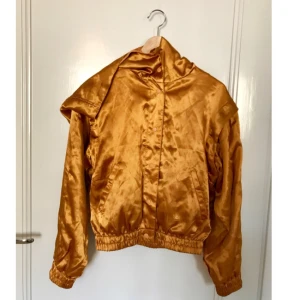  - Glammigaste bomber-guldjackan ever, dessutom med mycket väldesignade löstagbara ärmar! 💥Den kan alltså lätt förvandlas till en ärmlös jacka/väst. Som grädde på moset har den även en LUVA! 👏🏻 En riktig blickmagnet för alla sommarhalvårets tillfällen. Denna darling måste få se dagens ljus oftare! Innerfoder, tryckknappar, sidenaktigt tyg, mycket bra skick. Storlek XS men passar garanterat även S och M. MONKI 😻😻😻