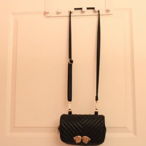 Väska / axelband väska  - En svart väldigt söt axelband väska med guldiga lejon huvud. Väldigt lätt att bära och kan fyllas i med flera saker. Kan levereras i Göteborg zon1 och 2 inom västtrafiks rese handlingar. Helst cash då jag inte har swish. Detta kan dock lösas. Lägg bud 