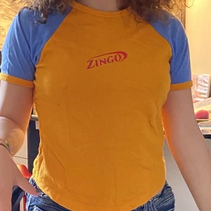 T shirt - En gul och blå t shirt med tryck där de står zingo. Frakt tillkommer