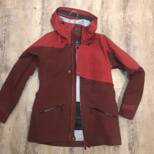 Haglöfs skidjacka - Haglöfs Khione 3L PROOF jacket Women, färg: Maroon red/ brick red. Storlek S  Jag säljer min skaljacka på grund av att jag vill ha en större storlek. Den är i mycket bra skick, inga fläckar eller skador. Jag köpte den i november 2019.  Bra andningsförmånga, och bra skydd för väder och vind. Är en perfekt skidjacka och med en tunn dunjacka under så håller man sig varm i riktigt kallt väder. Den har tillexempel: Hjälmkompatibel huva, ärmficka, ventilation och löstagbart snölås. Man kan läsa mer om den på outnorth.se.  Jag köpte den för 4495kr