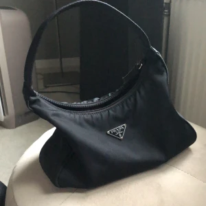 ÄKTA PRADA NYLON VÄSKA  - Säljer min vintage PRADA väska. Liten och söt. Beställd från the vintage bar för längesen. Man får även med en Prada tygpåse till väskan. Inköpt för 4900kr. Mått (ungefärligt) : L: 22 cm, H: 14 cm, D: 7 cm 