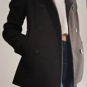 Mörkgrå kappa strl 34 - En mörkgrå kappa från h&m. Tyget är polyester och viskos. Kappan är välbehållen och i fint skick. Skön passform, framhäver former på ett smickrande vis, speciellt med kappan knäppt. Den är dock för liten för mig nu. Väldigt varm och skön, perfekt vår & höst jacka Nypris 599