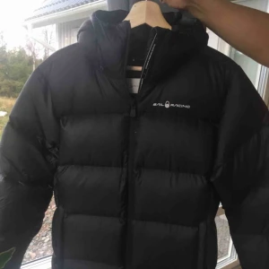  - Sail Racing pufferjacka. Aldrig använt, med prislappen kvar. Den är för stor för mig därav jag säljer den. Ord:pris 3800 kr.  Med luva och så lätt att bära! 