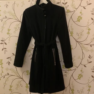 Höst/vinterkappa - Svart kappa från vero moda i storlek S! Köpt för två år sedan men sällan använd så den är i väldigt bra skick. Knäpps med dragkedja och knappar och med skärp i midjan. 