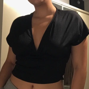 Svart tröja/blus - Svart V-ringad tröja med resår (skrynkligt)längst ner på baksidan. Oanvänd. Säljes pga ingen användning. Köparen står för frakt!