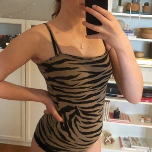 tigerbody - svinsnygg body i gråbrunt och svart trendigt tigermönster! kan bäras som den är med byxor eller ovanpå tex en svart polo, supersnyggt! justerbara axelband och knäppning i grenen. inte string.