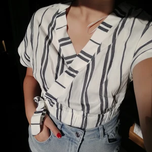  - Vit och blå randig blus med resår i midjan, den har även ett snöre i midjan som man kan knyta men det har ingen påverkan på hur tajt blusen blir. Den är helt oanvänd och ny med lappen kvar