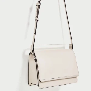  - Snygg vit väska från Zara, kan bäras som axelremsväska eller som clutch. Häftig modell med metall detaljer och premium fusk läder. Kommer med Zaras dust bag. Mått: 18x28x8 cm   Ny!  Frakt tillkommer.