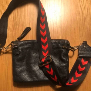  - Väska från other stories  Svart kuvert, med axelrem med röda detaljer som går att byta ut. 