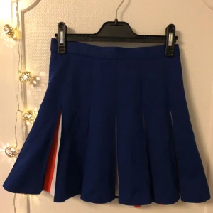  - Underbar cheerleaderkjol i mörkblått, vitt och orange med dragkedja och knäppning i bak. Storlek XS/S. 80kr + ev. fraktkostnad via Swish
