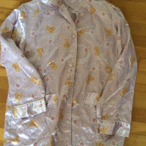 Satinöverdel med nallar - Världens sötaste överdel till pyjamas i satin. Ljuslila med blommor och nallar. Sparsamt använd. Storlek S men passar M också. Priset är inkl vanlig frakt 🐻