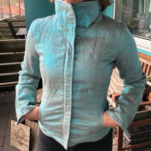 Blåskimrande vårjacka - En ball vintagejacka, perfekt nu till våren! I bra skick, något ”skrovlig utsida” men det är en del av designen. Väldigt snygg både öppen och stängd. Köparen står för frakt.