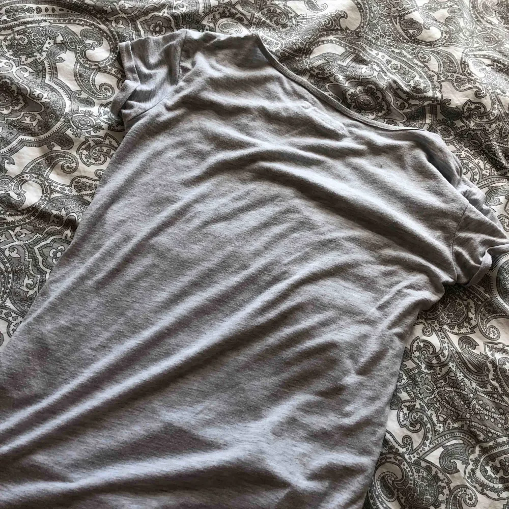 Det är en grå tröja med en liten ficka på som är mönstrad med blommor🥰 . T-shirts.