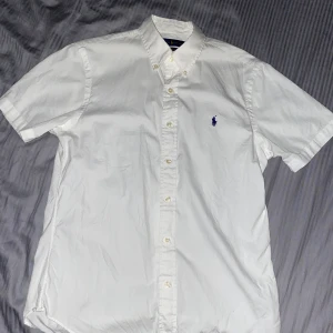 Polo Ralph Lauren Kortärman Skjorta M - Köptes midsommaren 2019 då jag endast använde den. Säljes för att den är tajt runt armarna då min omkrets är 44.5cm. Nyskick och passar medel personen.                                                                           Köptes för: 999kr