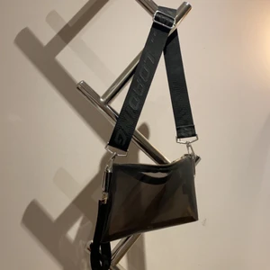 Genomskinlig svart väska - En supercool genomskinlig väska med ett coolt tjockt reglerbart axelband som går att ta av. Den har några enstaka fläckar som borde gå att tvätta bort. Kontakta vid intresse eller fler frågor✨✨ Köparen står för frakt.