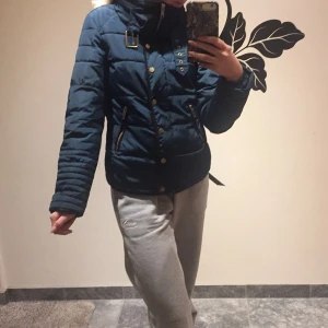 Jacka strl.34 - Jacka med snygga detaljer, bland annat på armbågarna och vid halsen. Blixtlås och andra knappar är i guld. Färgen på jackan speglar inte riktigt bilderna, jag tycker den är grön, blå åt de mörkare hållet. Blixtlåsen har fastnat lite i jackan som man kan se på bild 3 men går att använda eller om man vill, enkelt laga. Köpare står för frakt eller så kan jag mötas upp i Lund. 150kr + frakt eller högre bud.