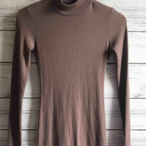  - En lång töjbar mörkbeige klänning från NA-KD i XS men funkar även för en S! Perfekt till festtillfällen eller nyår och värmer riktigt bra. Har använts max 2 gånger, köparen står för frakt 25kr😊