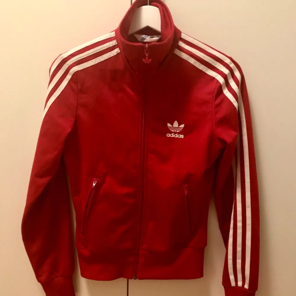 Röd Adidas tröja/track jacket/jacka, står storlek 32 i den men den är mer som en 34 enligt mig. Det är två jättesmå hål ovanför loggan fram, annars i perfekt skick🍎 . Hoodies.