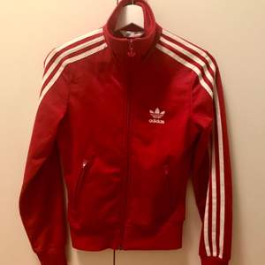 Röd Adidas tröja/track jacket/jacka, står storlek 32 i den men den är mer som en 34 enligt mig. Det är två jättesmå hål ovanför loggan fram, annars i perfekt skick🍎 
