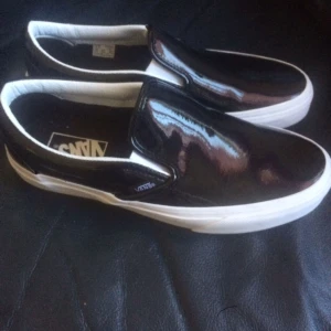  - Ett par svarta lackade Vans Slip On i nyskick, se bilder! Glansigt svart material med vita detaljer, jättefina! Nypris 800, mitt pris 450! Originalkartong medföljer! 