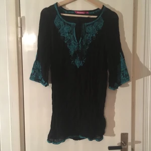  - Fin svart tunika från Indiska med turkosa detaljer, i tunt, transparent tyg.  100% viskos.  Knappt använd.  Har swish, köparen står för frakt.