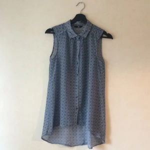  - Armlös skjorta i tunt, lite transparent tyg med ljusblå mönster.  Storlekslappen är bortklippt men skulle gissa på XS/S. Den är lös i passformen och lite längre baktill. Pris inkl frakt. 