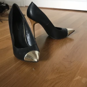 Svarta klackar med guld design  - Höga klackskor som har används bara några gånger. Perfect if you want the boujee and classy look. Kan använda de till jobbet eller finsitning 