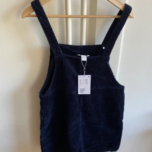 Hängselklänning Monki - Marinblå hängselklänning i Manchester-material. Aldrig använd. Slutar strax ovanför knäna på mig som är 169cm. Kan mötas upp i Sthlmsområdet, annars står köparen för frakt.